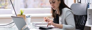 Female entrepreneur sitting at her desk doing manual calculations with a calculator trying to understand what her return on investment will be.